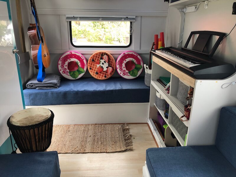 Little Musical Caravan inside front view with instrument cabinet on the right, pink and orange cushions and guitar hanging on left wall