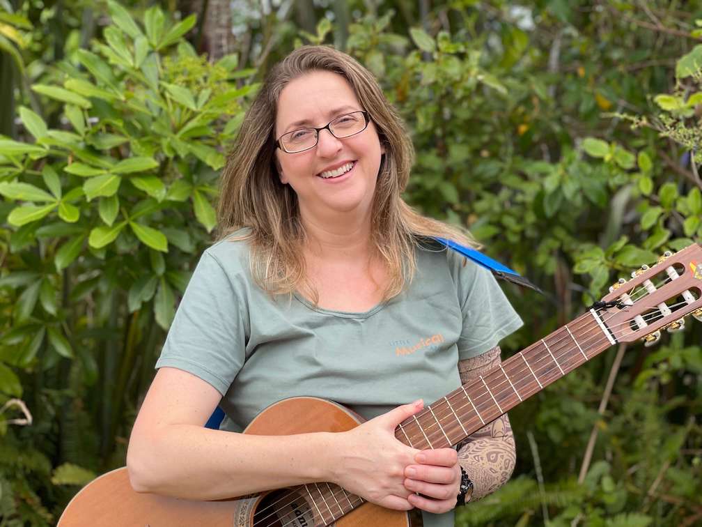 Emily smiling at the camera holding a guitar with greenery in the background