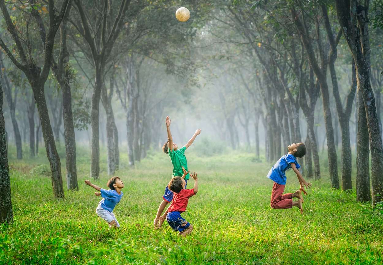 4 boys jumping in the grass and framed by trees